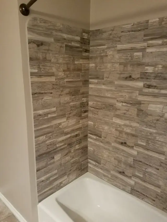 Bathroom shower walls covered in grey and white stacked stone-look tile